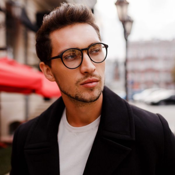 Confident young man in full suit  looking away while standing outdoors  in european city. Wearing eyewear. Stylish hairstylr.